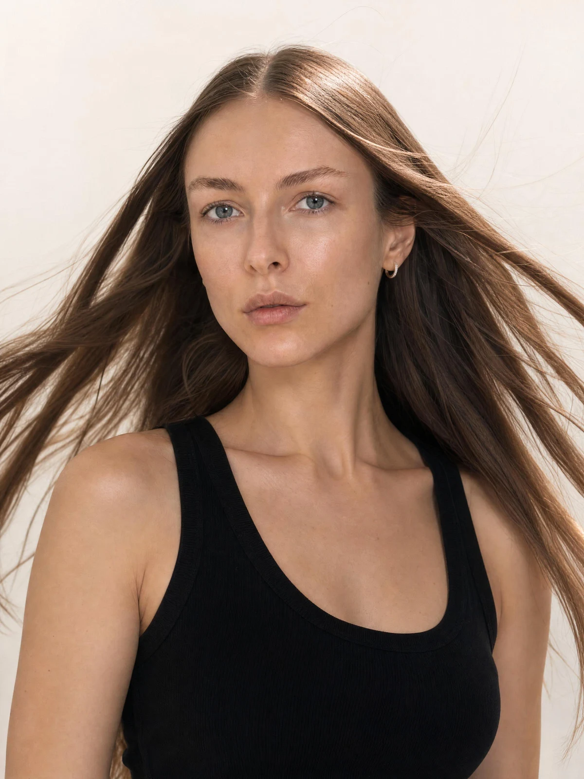 Model in a black tank with windswept hair against a light studio background
